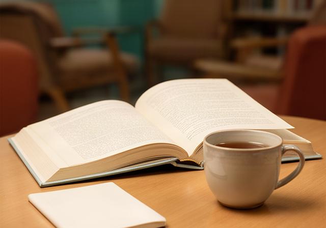 Tavolo di lettura con libro aperto, taccuino e luce soffusa in una sala del circolo